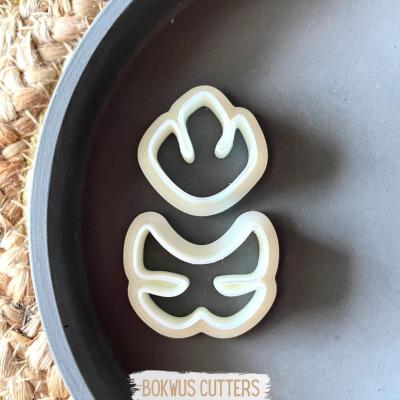 Dois cortadores de biscoitos brancos em forma de patas, num prato escuro em cima de juta.