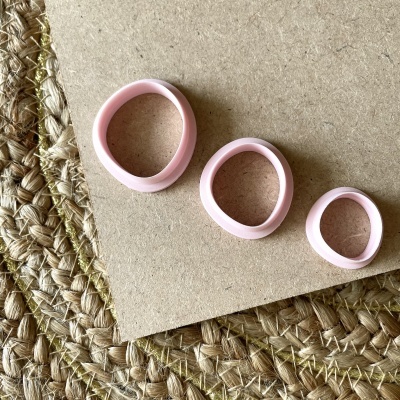 Três anéis de silicone rosa em diferentes tamanhos sobre superfície bege e tapete trançado.