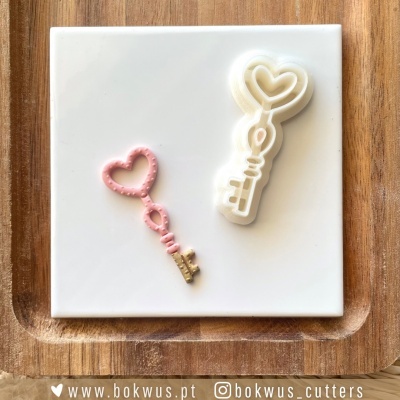 Dois cortadores de biscoitos em forma de chave com coração sobre azulejo branco e bandeja de madeira