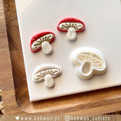 Cortadores de biscoito em forma de cogumelos vermelhos e brancos sobre superfície branca e madeira.