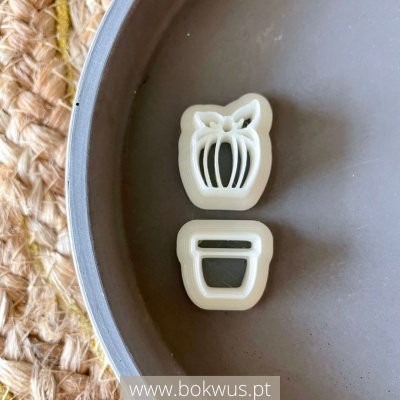 Cortadores de massa plásticos em forma de vaso com planta sobre superfície cinzenta e base trançada.