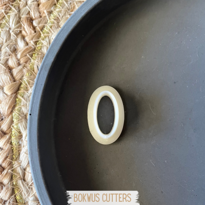 Anel branco em forma de O em plateau preto sobre mesa com toalha de palha entrelaçada