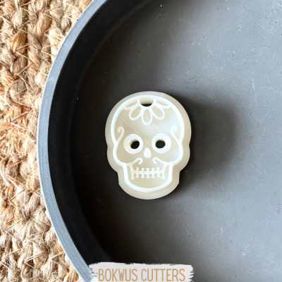 Cortador de biscoitos em forma de caveira branca com padrão floral sobre prato cinza.