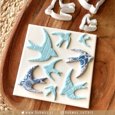 Matriz de cortadores em forma de andorinhas em branco com padrões em azul, sobre base branca e tabuleiro de madeira
