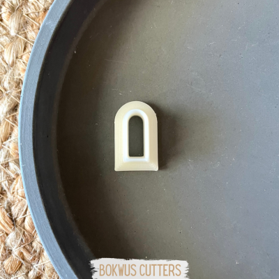 Cortador branco e preto em forma de arco numa bandeja cinzenta sobre superfície de ráfia