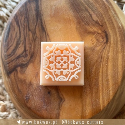 Barra de sabonete quadrada cor pêssego com padrão branco sobre base de madeira circular