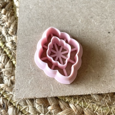 Cortador de biscoitos em forma de rosa cor-de-rosa sobre superfície de cortiça e tapete de fibras naturais