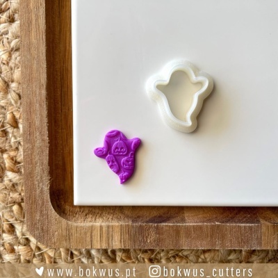 Cortante fantasma branco com amostra de massa roxa decorada, sobre base branca e tábua de madeira.