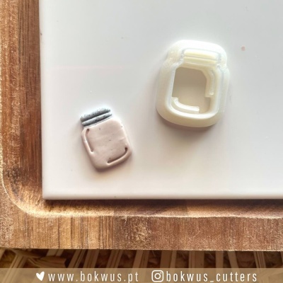 Cortador de massa em formato de frasco com massa moldada ao lado, sobre superfície branca e base de madeira