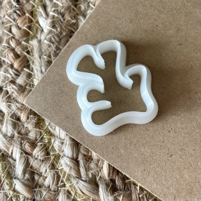 Forma de cortar biscoitos em forma de pata de animal branca sobre cartão castanho e tapete de fibras naturais.