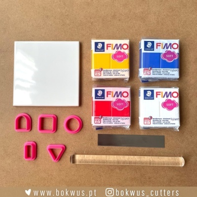 Blocos de massa FIMO Soft coloridos, cortadores rosa, base branca, régua preta e rolo de madeira num fundo castanho.
