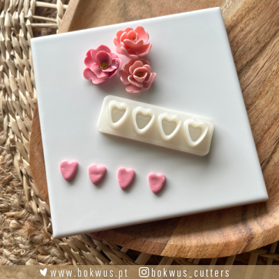 Molde de silicone com cavidades em forma de coração e peças rosas modeladas sobre tabuleiro branco