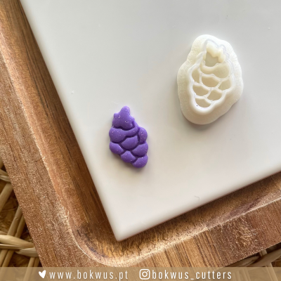 Cortador branco de plástico e peça roxa em forma de cacho de uvas sobre bandeja de madeira