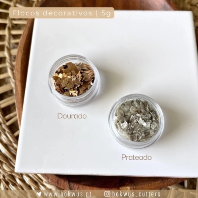 Dois frascos com flocos decorativos dourados e prateados sobre superfície branca