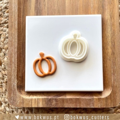 Dois cortadores de biscoitos em forma de abóbora num fundo branco sobre tabuleiro de madeira.