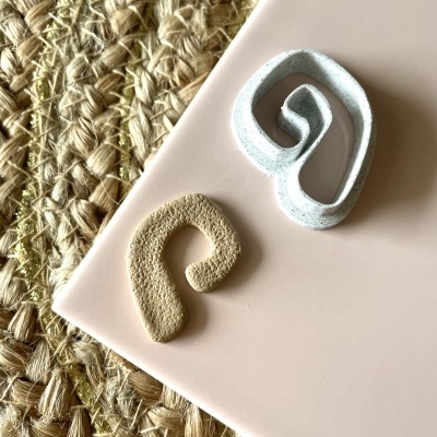 Dois objetos decorativos em espiral em cima de superfície rosa clara junto a tapete de fibras naturais