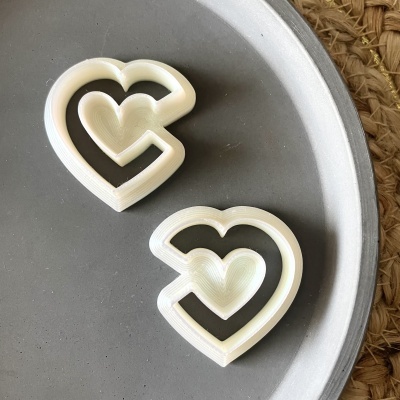 Dois cortadores de biscoitos em forma de coração brancos sobre superfície cinzenta redonda.