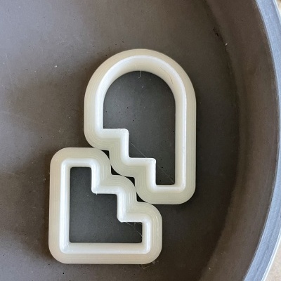 Moldes de plástico brancos com formatos geométricos colocados numa superfície cinza.