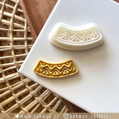 Cortadores de massa em formato meia-lua com padrão geométrico, branco e amarelo, em placa branca sobre textura de madeira e tecido trançado.