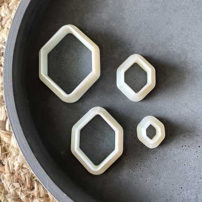 Quatro moldes de plástico em forma de losango, de tamanhos diferentes, sobre prato preto liso.