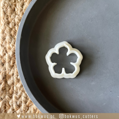 Cortador de biscoitos em forma de flor branco sobre prato cinzento e superfície de ráfia.