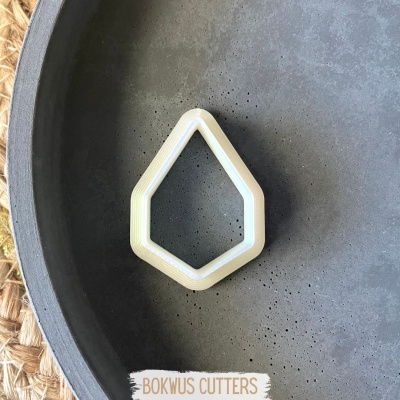 Cortante para bolachas em forma de gema, branco, sobre superfície preta e suporte castanho