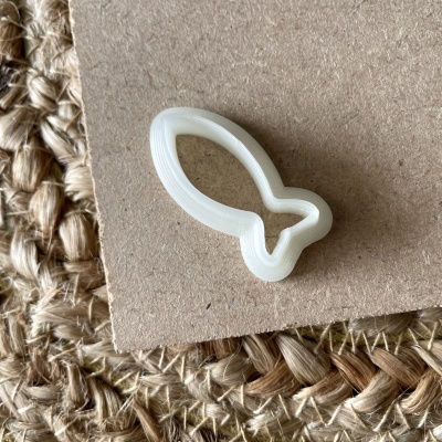 Cortador de biscoitos plástico branco em forma de peixe sobre cartão e base de juta