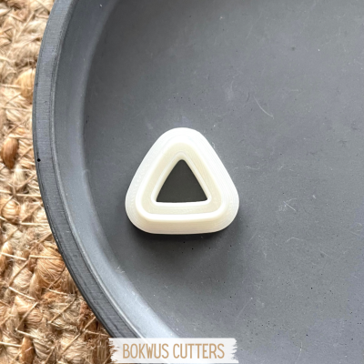 Cortador triangular branco sobre prato cinzento em superfície tejida com etiqueta BOKWUS CUTTERS