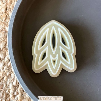 Cortante para bolachas em forma de folha bege com contorno branco num prato castanho escuro.