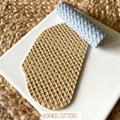 Rolo texturizador azul claro com padrão geométrico e massa modelada bege sobre placa branca