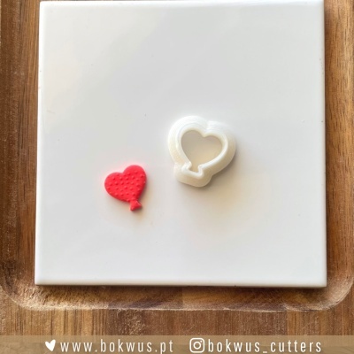 Cortador de biscoitos branco em forma de coração e coração vermelho em massa sobre superfície branca quadrada
