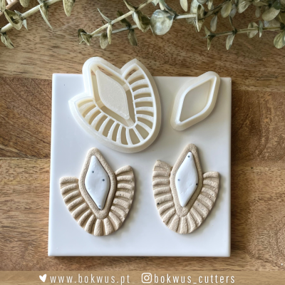 Cortadores de massa creme em forma de folhas com relevos sobre base branca em mesa de madeira.