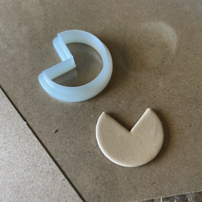 Clip plástico translúcido branco e peça de silicone bege em forma de 'pizza' sobre superfície castanho clara