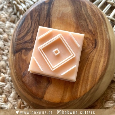 Cortante quadrado de massa cor de pêssego com padrão geométrico em relevo sobre base de madeira redonda