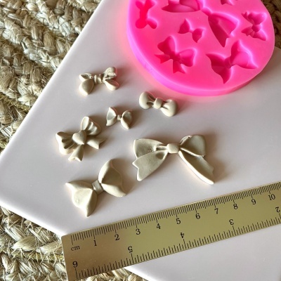 Molde de silicone rosa com formas de laços e laços brancos feitos ao lado de uma régua