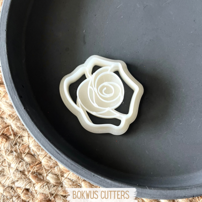 Forma branca de cortar biscoitos em forma de rosa sobre superfície preta redonda