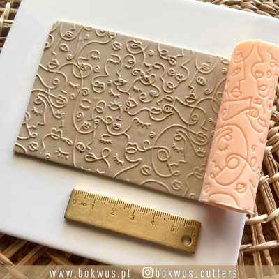 Rolo de textura cor de laranja e impressão em papel castanho com padrão abstrato e régua dourada.