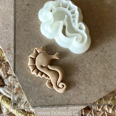 Molde branco de silicone e peça castanha em forma de cavalo-marinho sobre superfície castanha