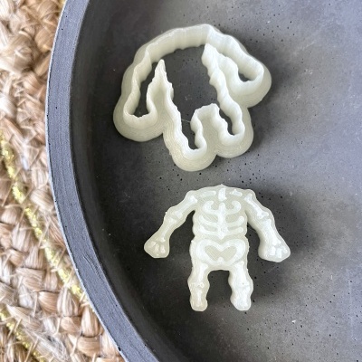 Dois cortantes de plástico para bolachas, um em forma de cachorro e outro de esqueleto, sobre prato cinzento e tecido trançado
