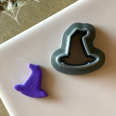 Cortador de massa em forma de chapéu de bruxa preto com peça roxa ao lado e texto Halloween no fundo.