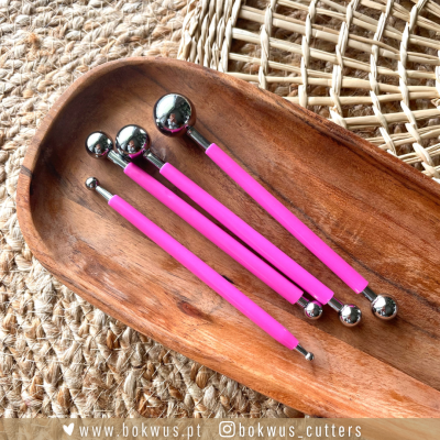 Ferramentas de modelagem com cabos rosas e pontas metálicas esféricas em travessa de madeira