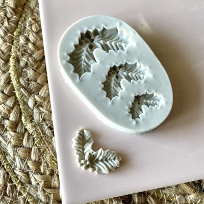 Molde de silicone branco em formato de raminhos de folhas de azevinho com ornamento branco e tapete bege