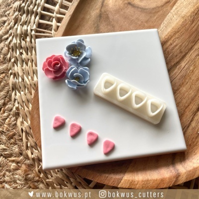 Cortadores de bolos em formas de flores e corações sobre placa branca em fundo madeira e tecido trançado