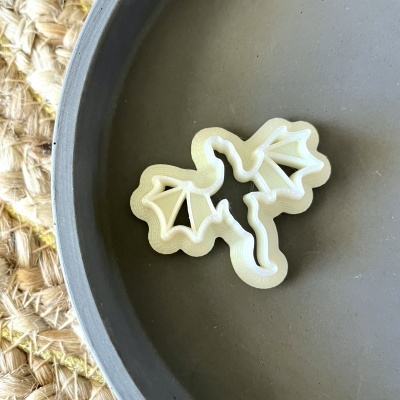 Cortador de biscoitos plástico branco em forma de dragão sobre prato cinza e tapete de fibras naturais.