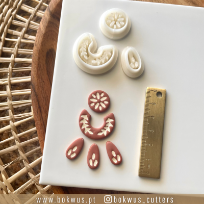 Cortadores para biscoitos em plástico branco com régua dourada ao lado sobre placa branca e base de madeira com padrão de cesto de vime