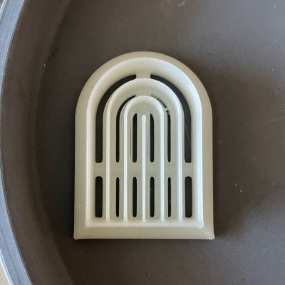 Peça plástica creme arqueada com aberturas sobre superfície cinza redonda