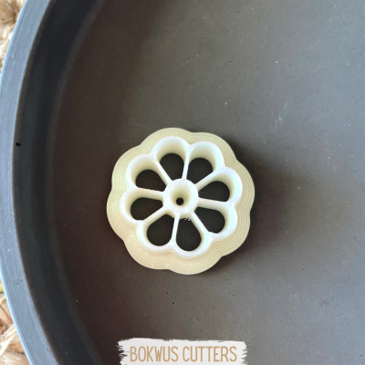 Cortador de massa em plástico branco formato flor sobre prato cinzento