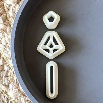 Três objetos geométricos brancos dispostos verticalmente numa base preta redonda sobre superfície de fibras naturais tecidas.