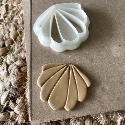 Cortador de biscoitos branco em forma de concha e massa dourada moldada semelhante sobre superfície castanho clara