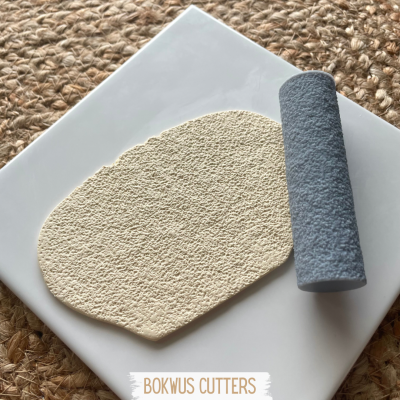 Base branca com massa bege granulada e rolo cilíndrico azul sobre superfície rústica